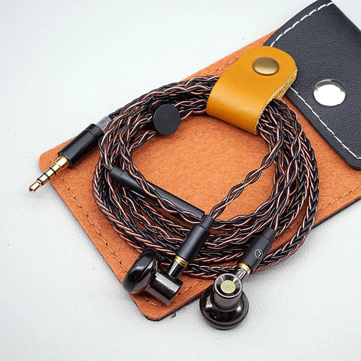 Fones de ouvido com fio pretos e marrom com cabo entrelaçado, sobre almofada marrom