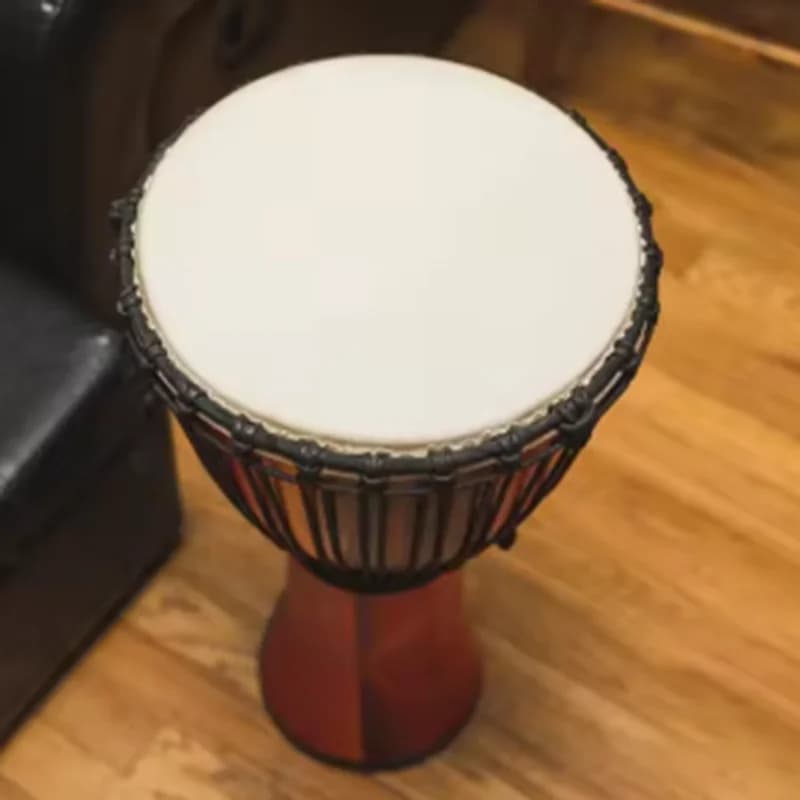 Djembe profissional com pele de cabra, corpo marrom e detalhes pretos, sobre fundo de madeira.