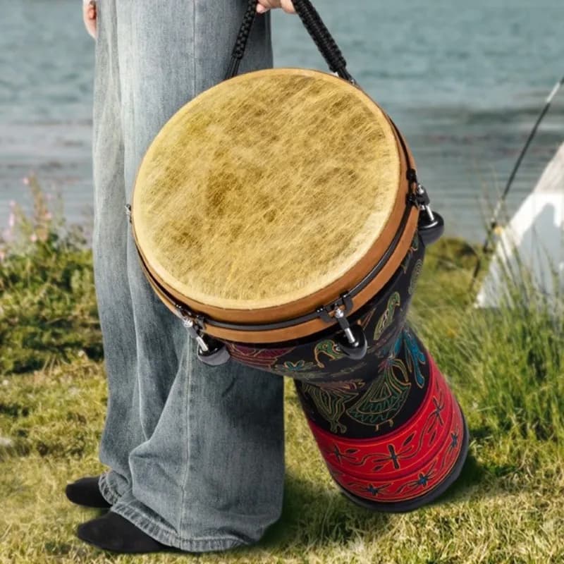 Djembe tradicional africano com padrões coloridos, segurado por uma pessoa em pé na grama