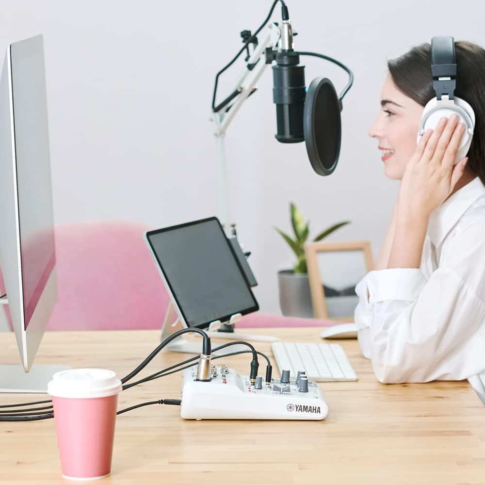 Mulher usando fones e microfone com mesa de som Yamaha AG03 MK2 branca para streaming e gravação