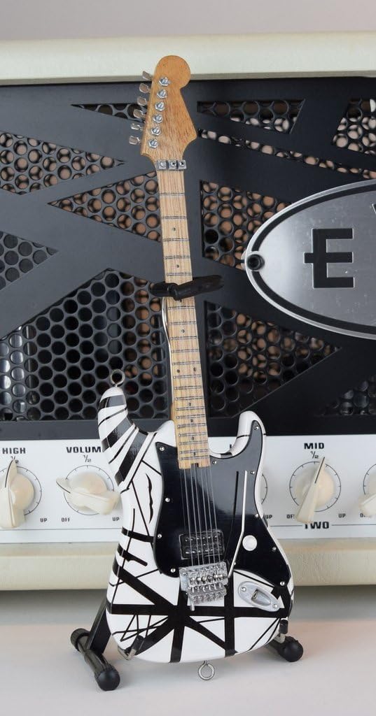 Mini guitarra AXE HEAVEN EVH003 branca com listras pretas sobre suporte diante de amplificador.