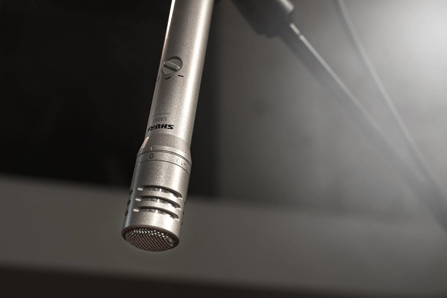 Microfone condensador Shure SM81-LC suspenso em suporte com iluminação ambiente