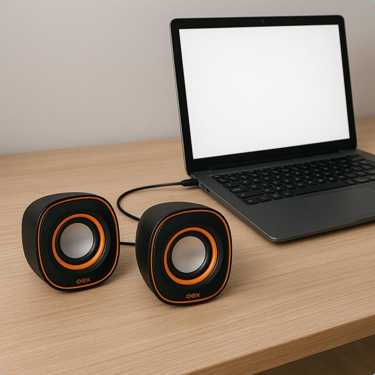 Caixas de som OEX SK100 conectadas a notebook, caixas pretas com detalhes laranja sobre mesa de madeira.