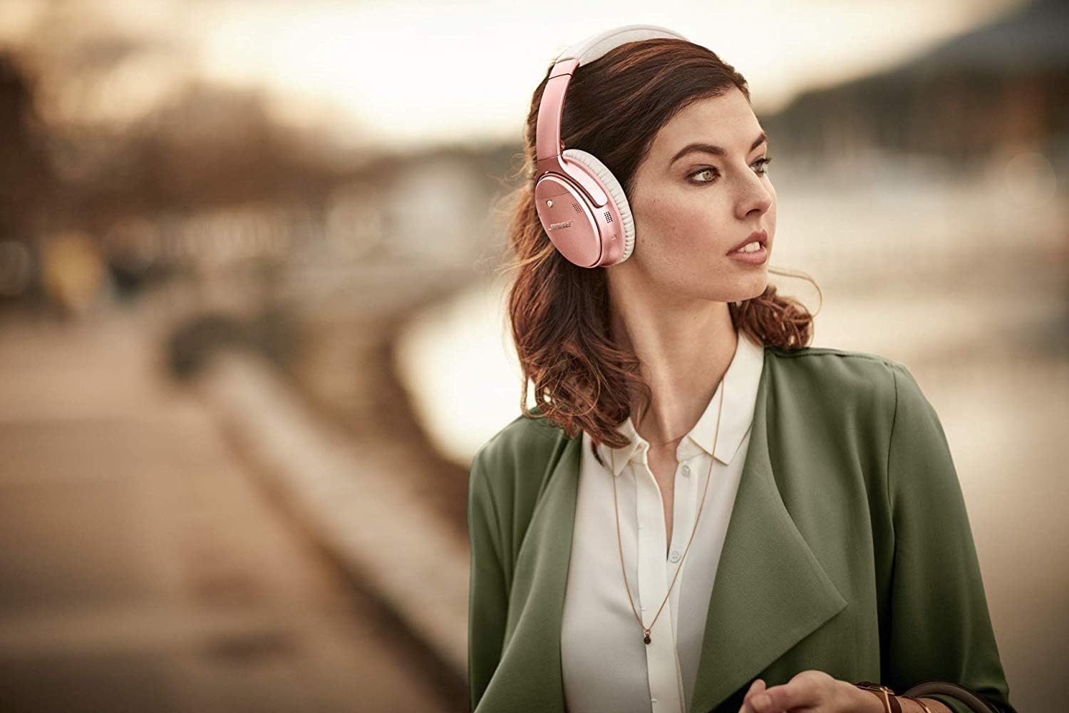 Mulher usando fones de ouvido Bluetooth Bose QuietComfort 35 II rosa com cancelamento de ruído ativo ao ar livre.