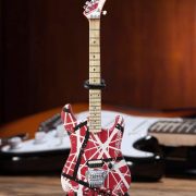 Miniatura decorativa de guitarra elétrica Axe Heaven EVH004 vermelha com listras brancas e pretas em suporte preto.