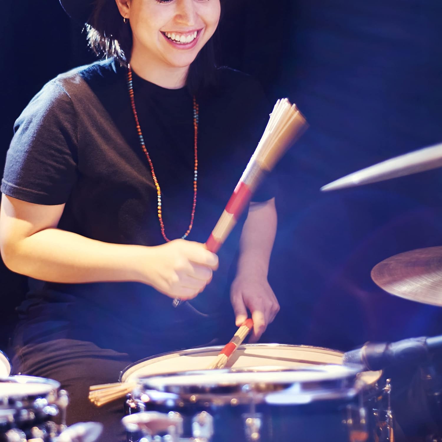 Mulher tocando bateria em palco usando varas de madeira vermelhas Meideal para jazz, folk e rock.