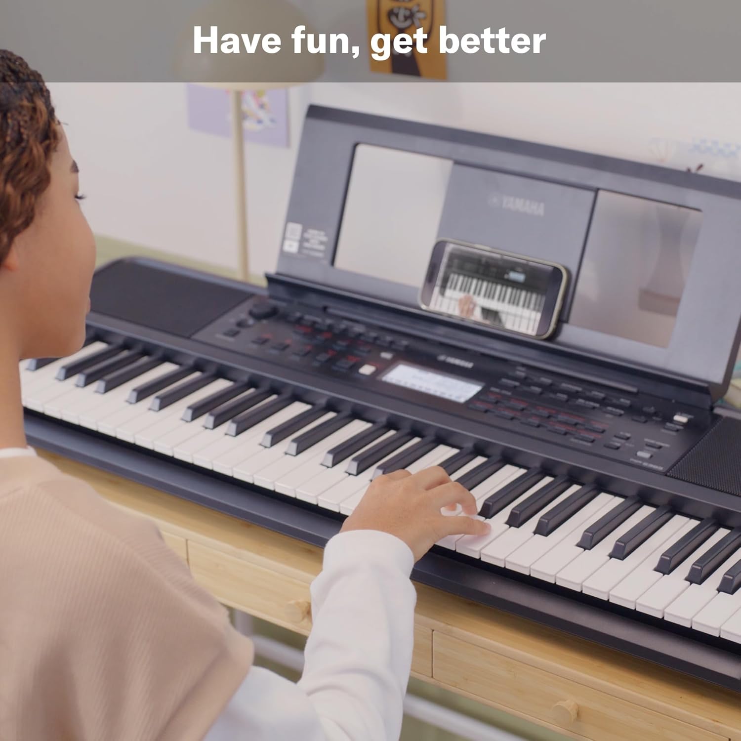 Pessoa tocando teclado Yamaha PSR-E383 com smartphone para aprendizado musical.