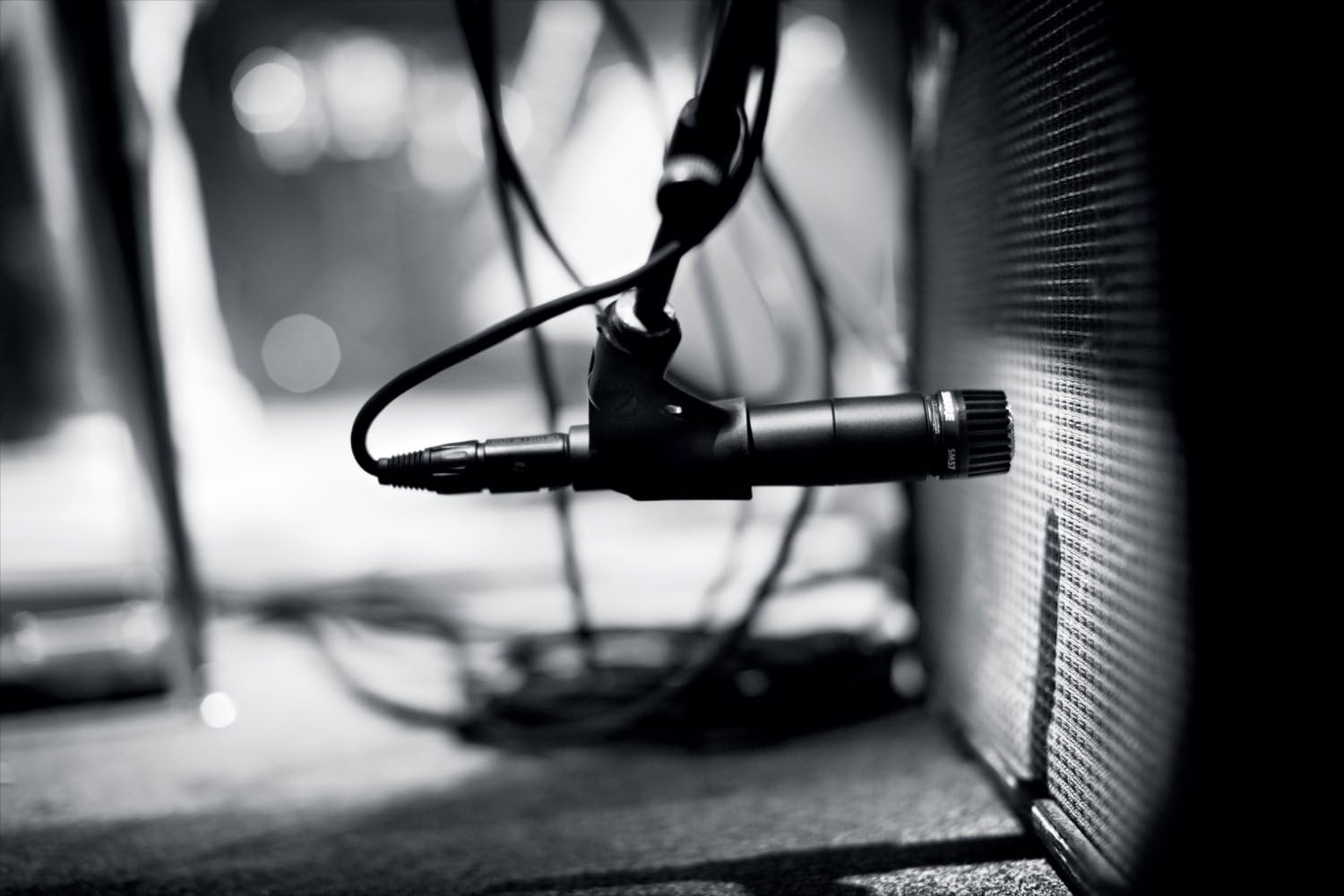 Microfone dinâmico Shure SM57-LC em uso com montagem de choque e cabo XLR próximo a amplificador, imagem em preto e branco.