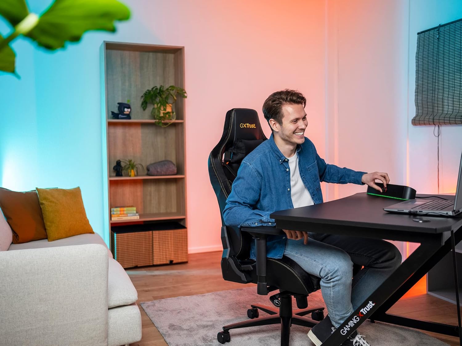 Pessoa usando computador com soundbar Trust GXT 619 Thor iluminado RGB em ambiente de trabalho moderno.