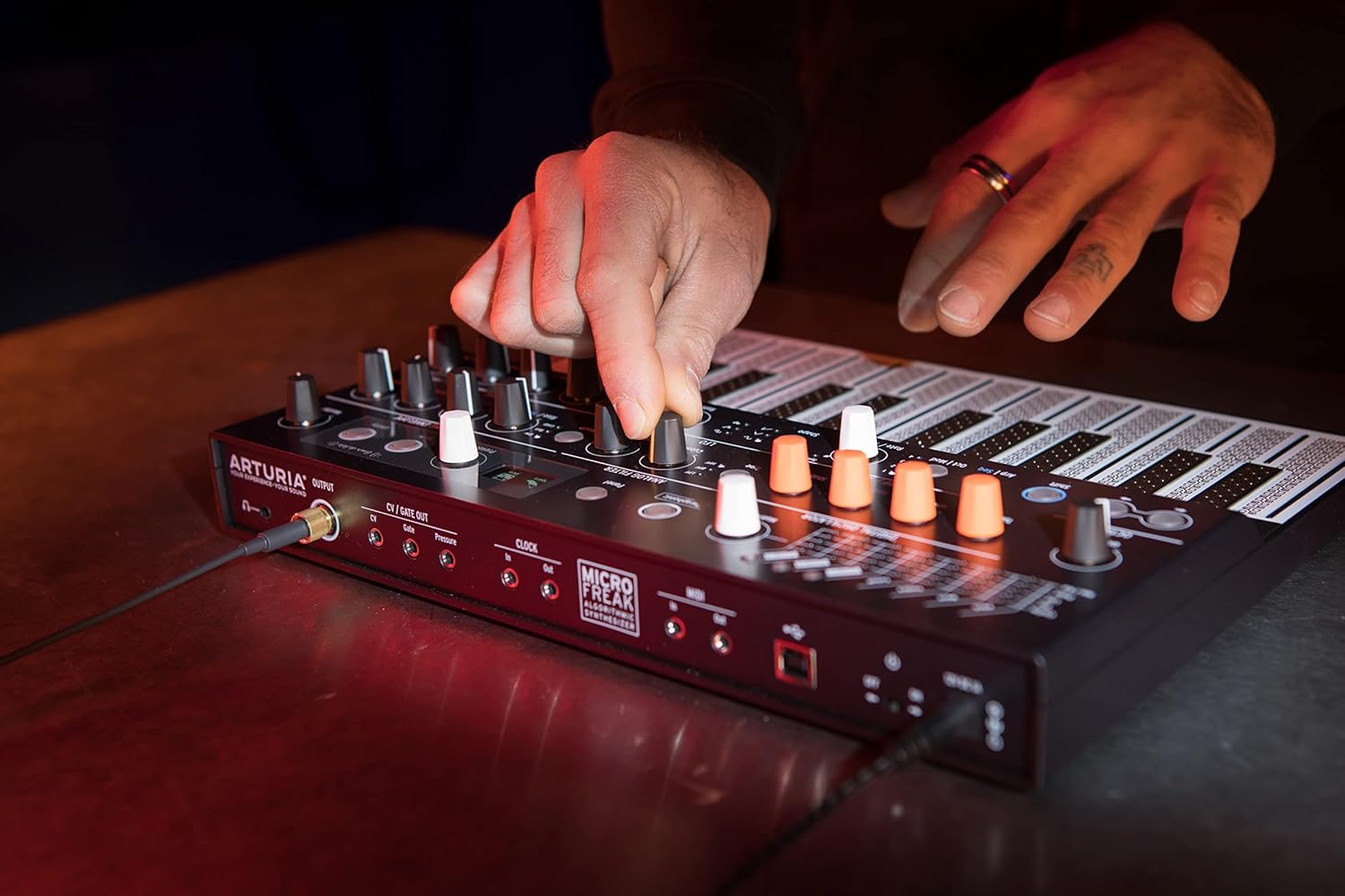 Usuário ajustando knobs do sintetizador Arturia MicroFreak com teclado PCB sensível à pressão e conexões CV/Gate e MIDI visíveis.