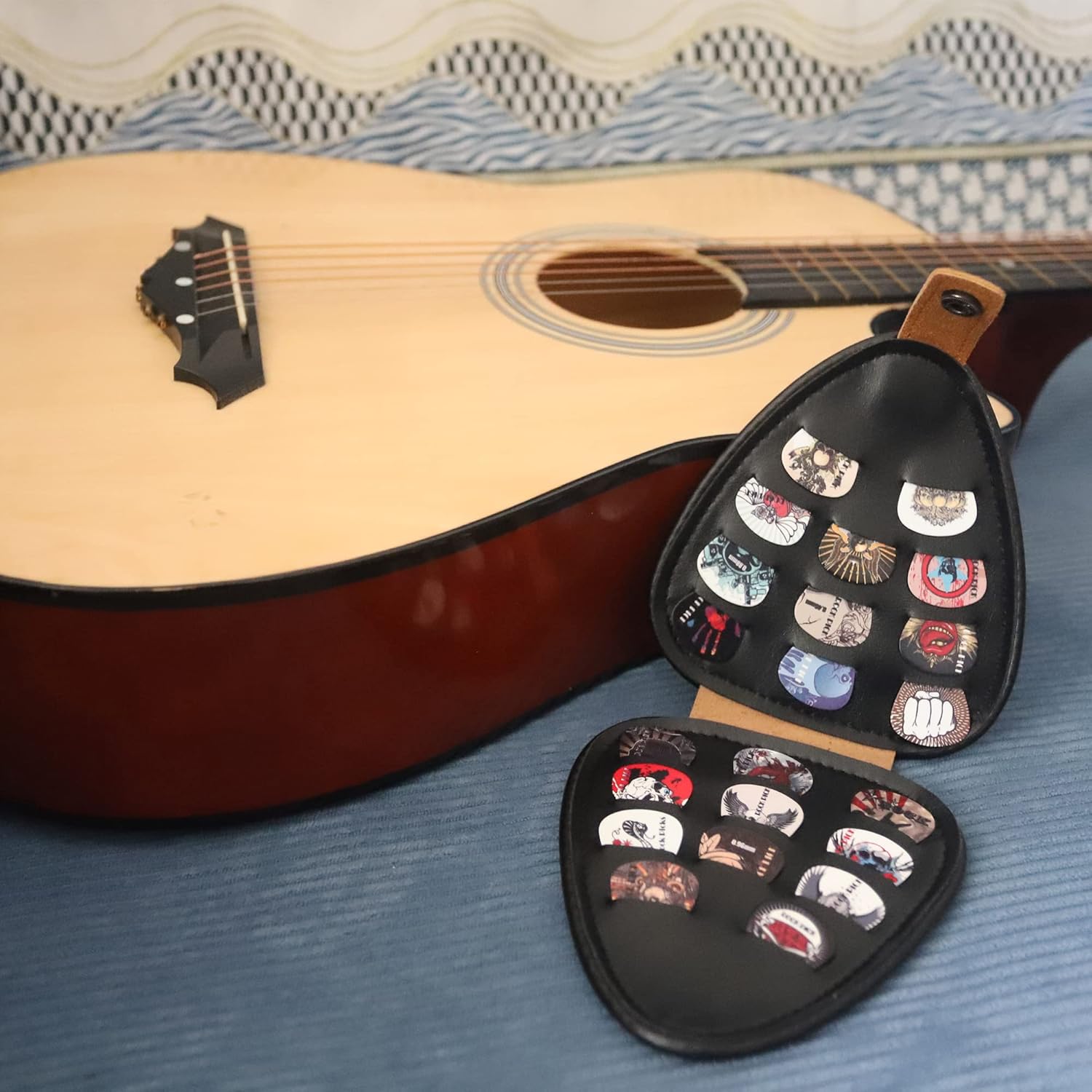 Estojo triangular em couro sintético marrom aberto com palhetas coloridas ao lado de guitarra acústica clara.