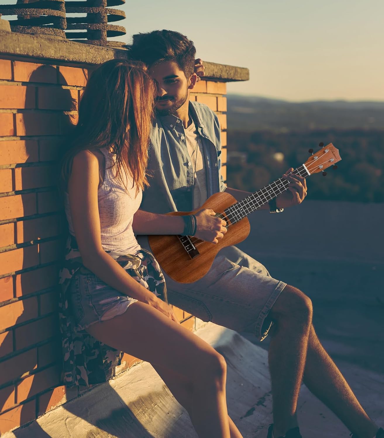 Casal jovem ao pôr do sol com homem tocando ukulele Ulumac de mogno sólido, ambiente descontraído e romântico