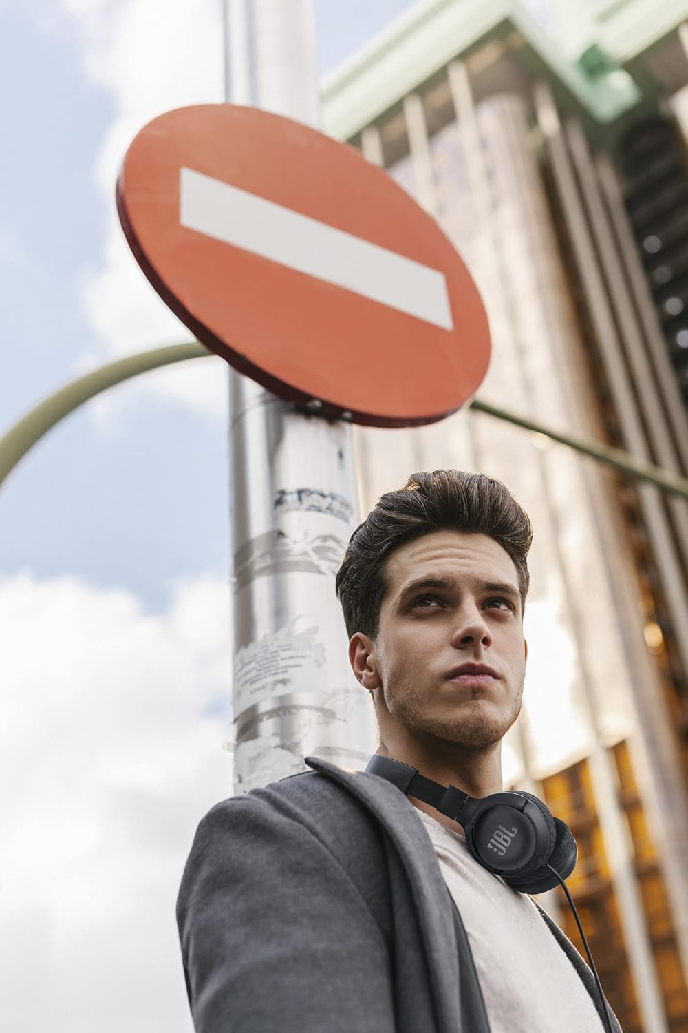 Homem usando fone JBL Tune 500 preto com fio pendurado no pescoço em fundo urbano