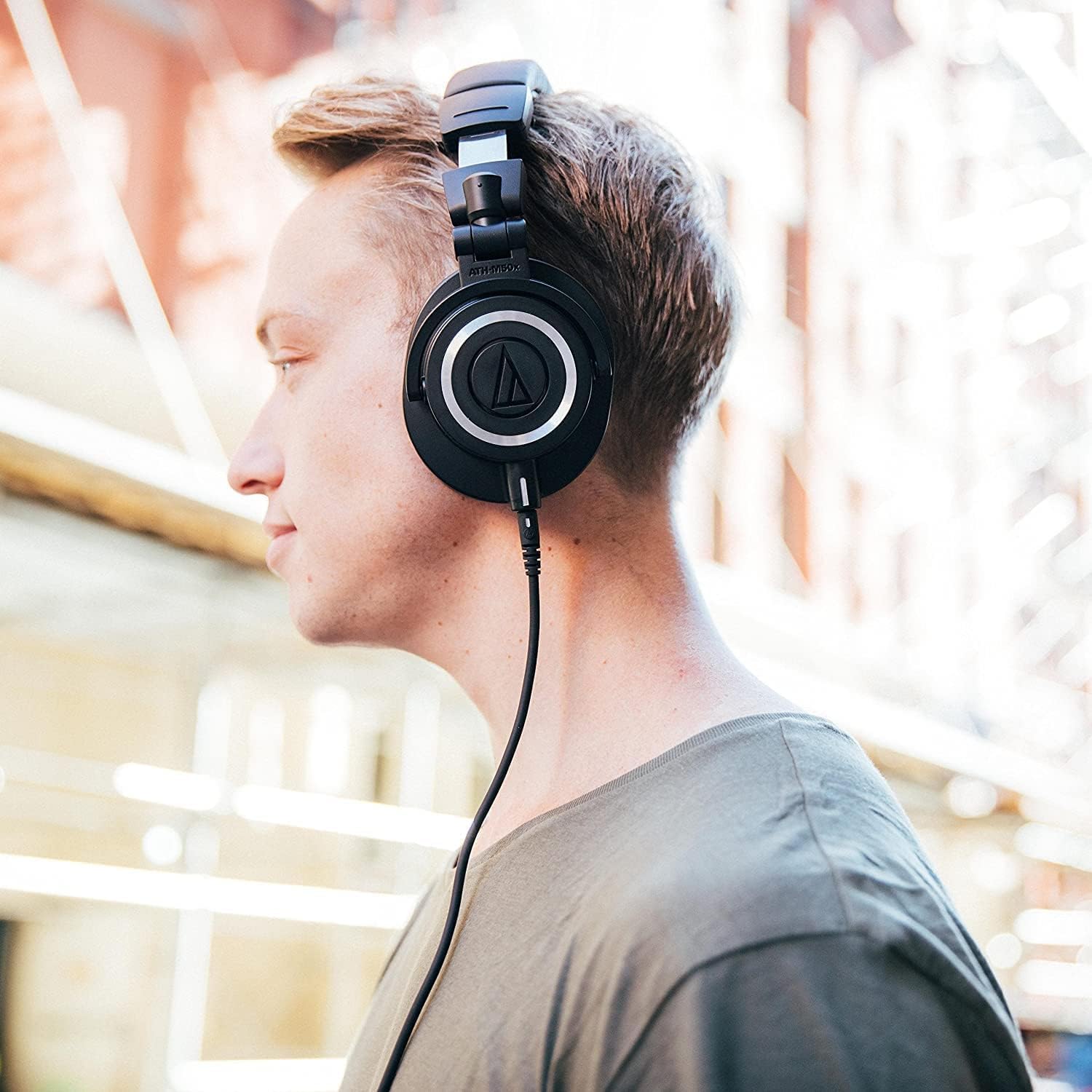 Homem usando fone de ouvido Audio-Technica ATH-M50x preto over-ear com fio em ambiente externo.