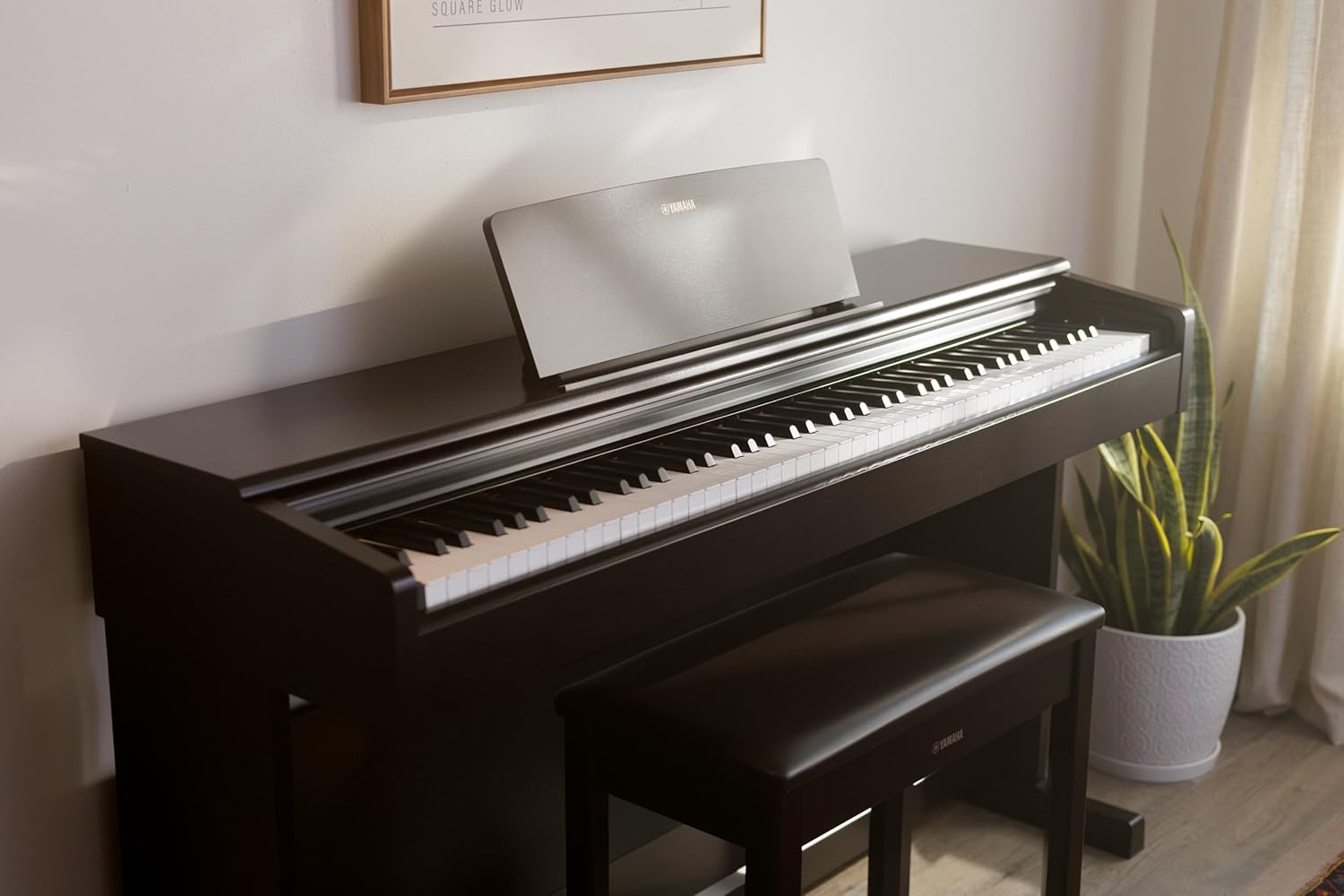 Piano Digital Arius YDP 145 B Yamaha preto em close lateral em ambiente interno com planta e luz natural
