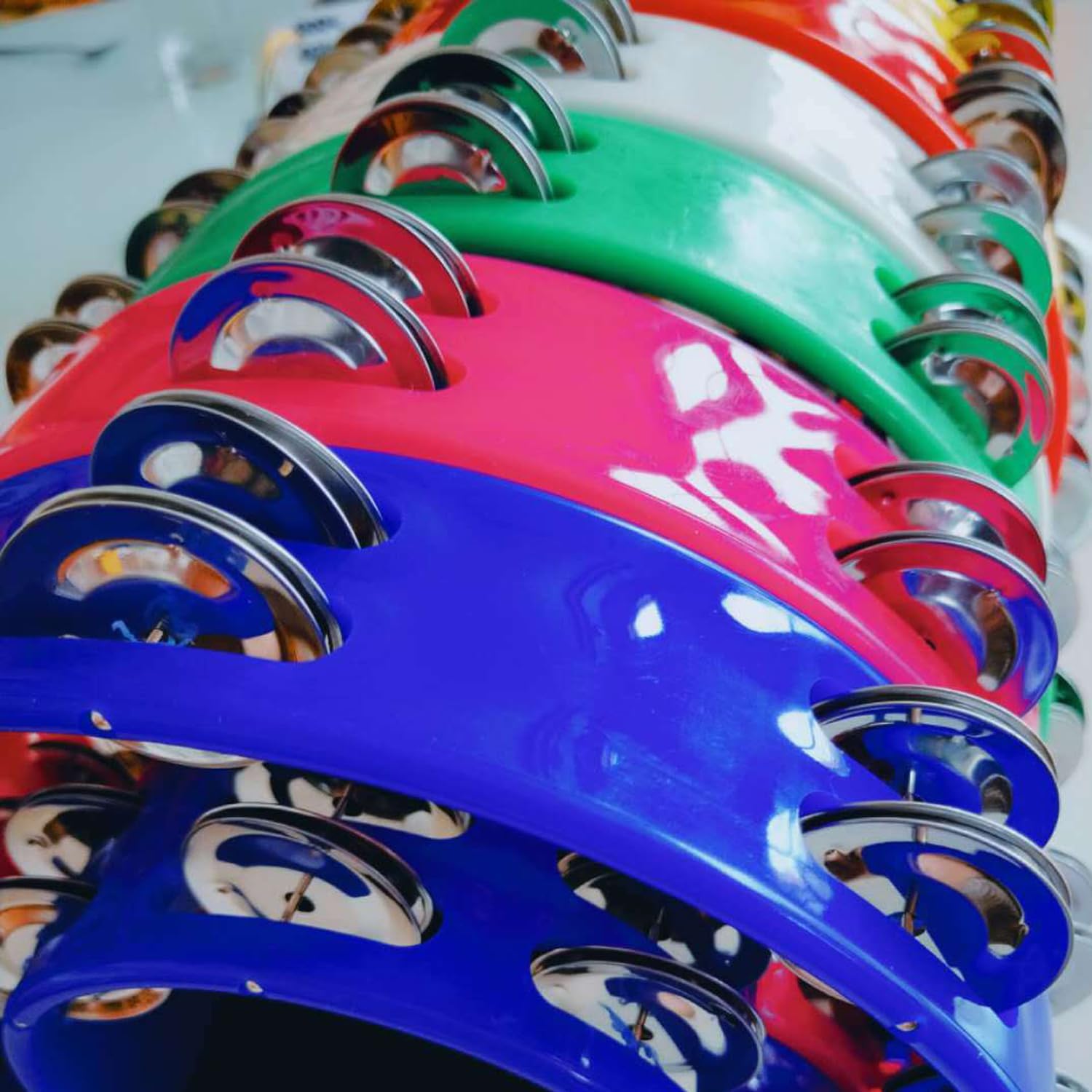 Detalhe dos címbalos metálicos prateados em vários pandeiros coloridos TENINYU Half Moon com alça ergonômica preta