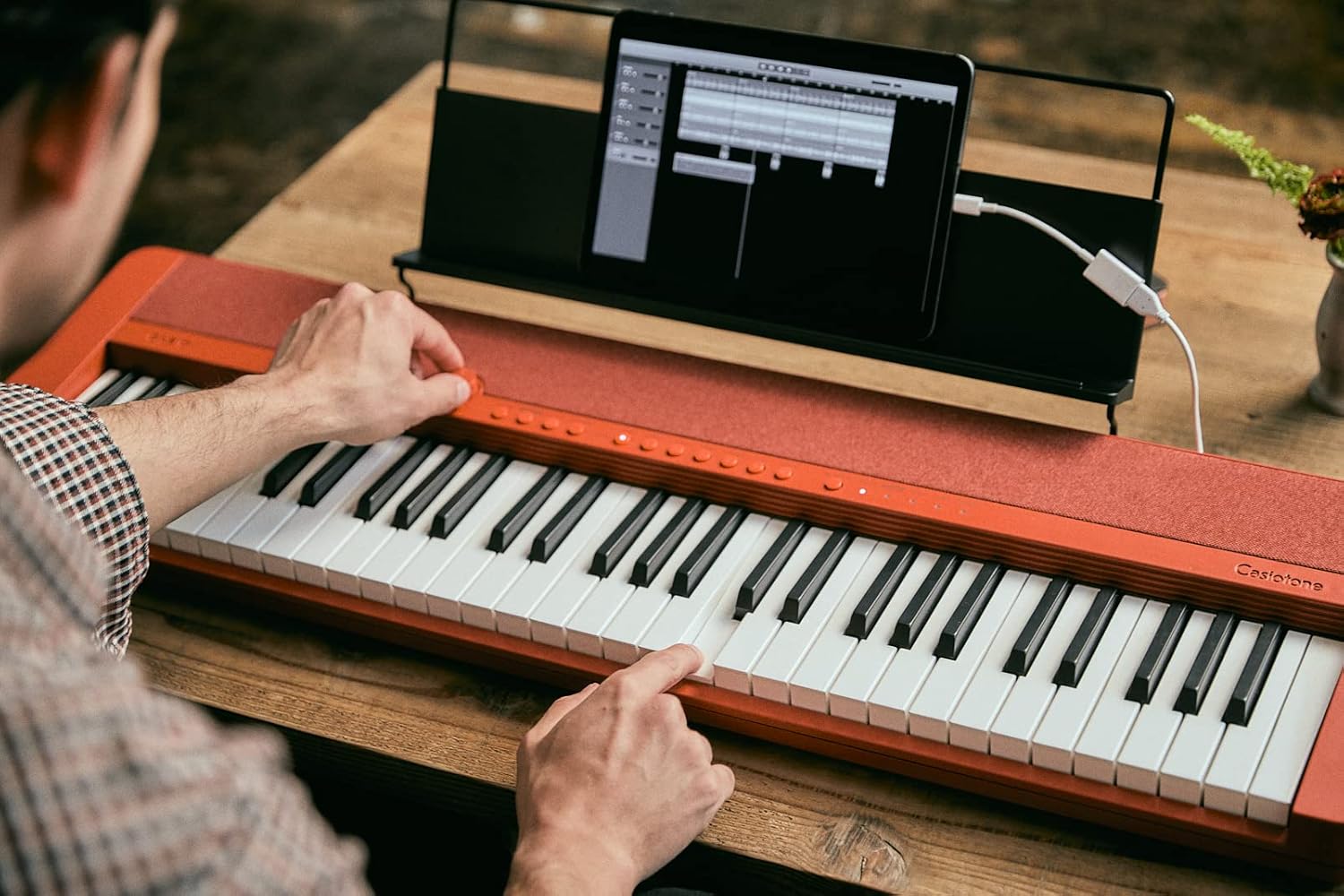 Pessoa tocando teclado Casio Casiotone CT-S1 vermelho com tablet conectado em suporte