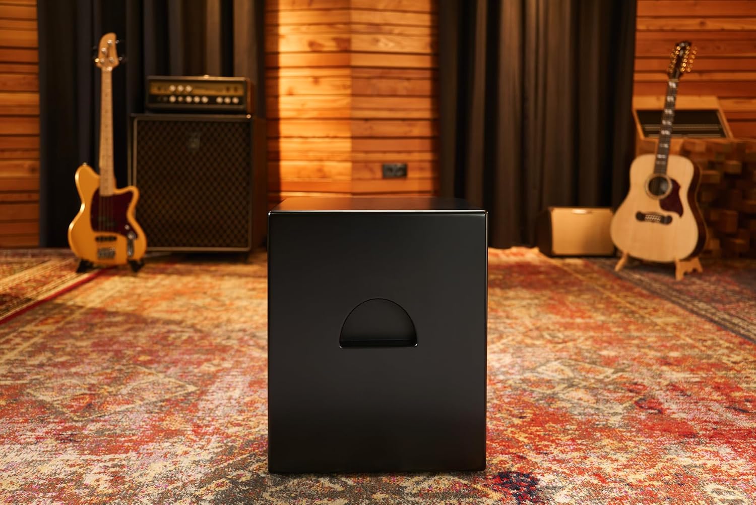 Cajon Meinl preto fosco com alça recortada em sala de música com instrumentos ao fundo