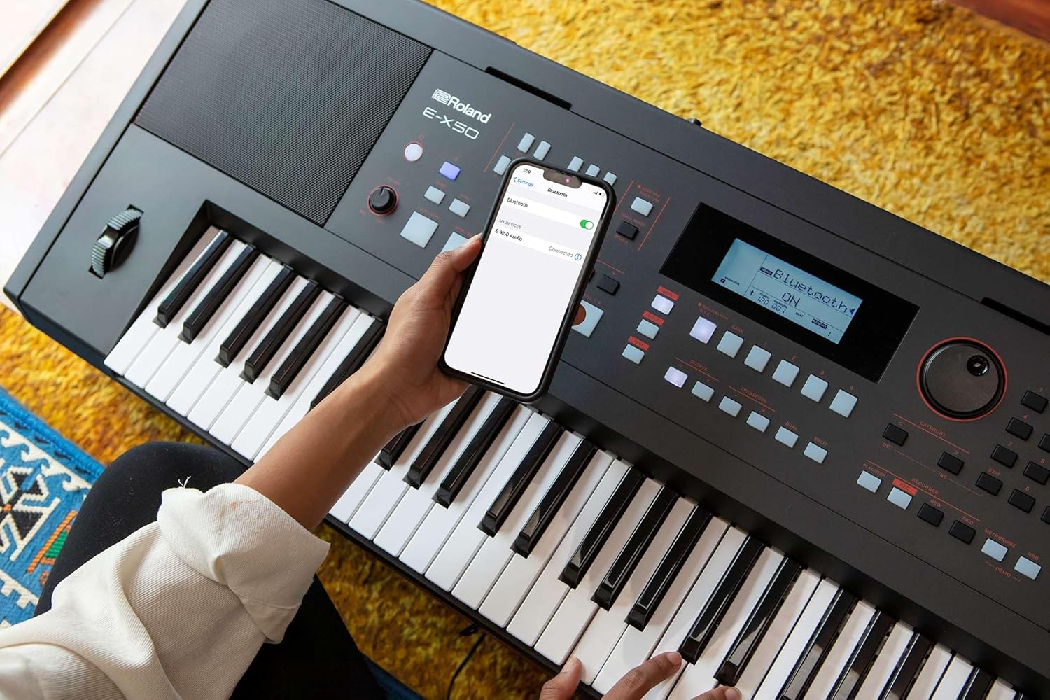 Teclado Roland E-X50 com conexão Bluetooth ativa e smartphone ao lado