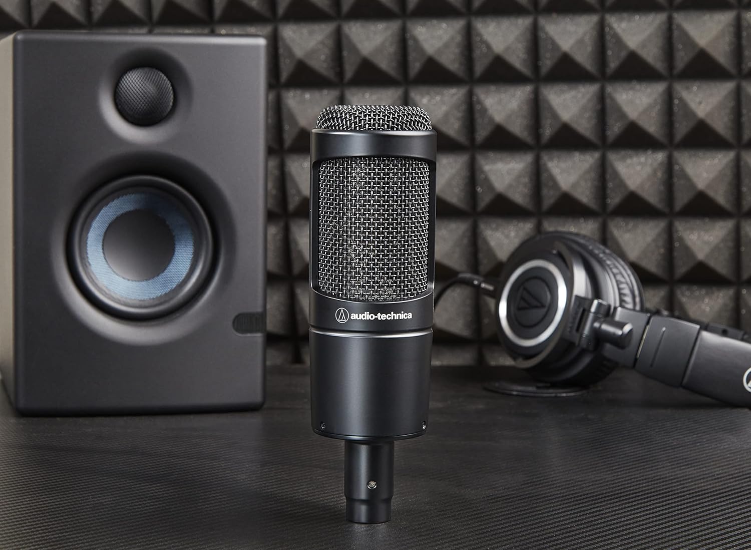 Microfone condensador Audio-Technica AT2035 em estúdio com monitor de áudio e fones de ouvido.