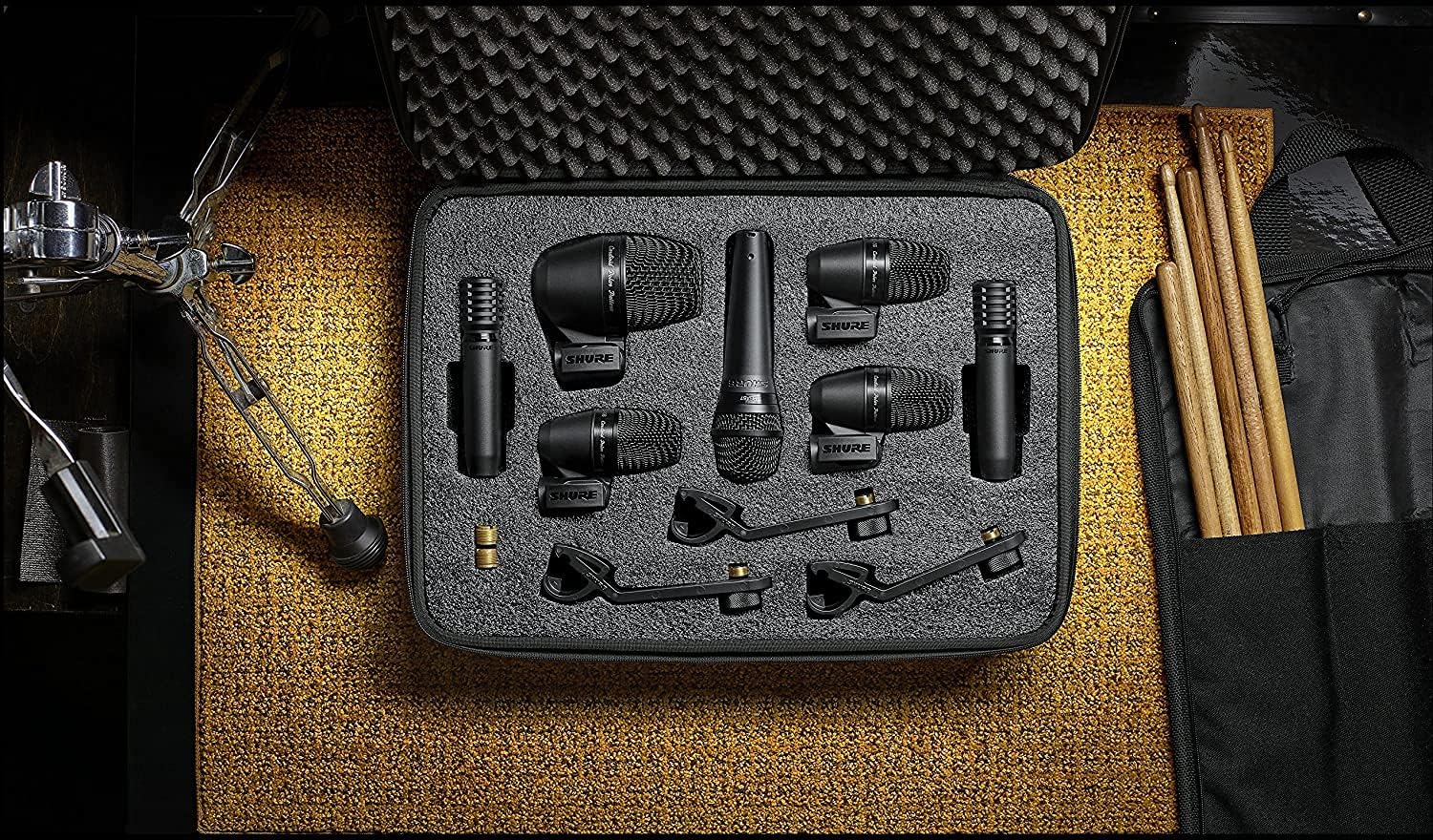 Kit de microfones Shure PGA DrumKit7 com acessórios em estojo preto e baquetas ao lado