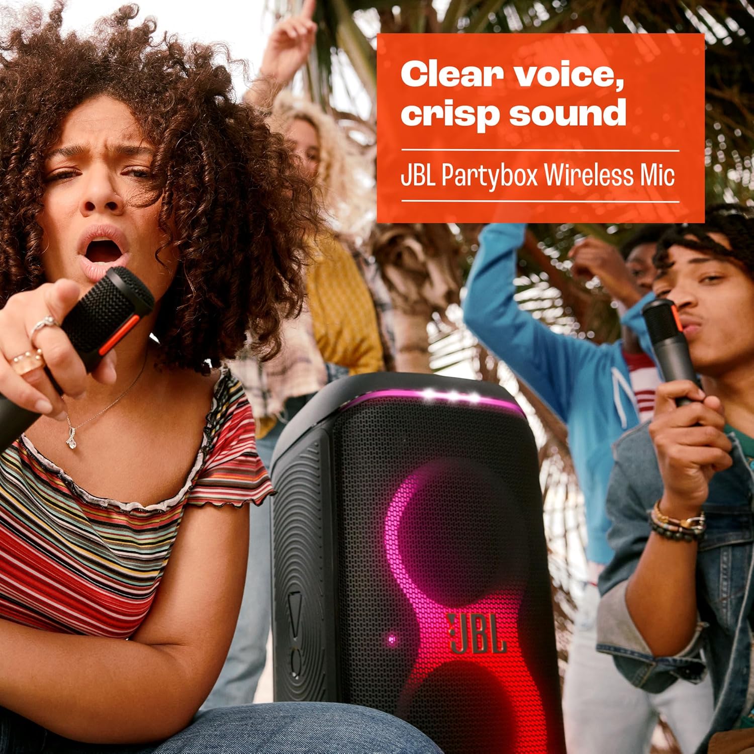 Pessoas em festa ao ar livre cantando com microfones sem fio JBL PartyBox e caixa de som com LEDs rosa