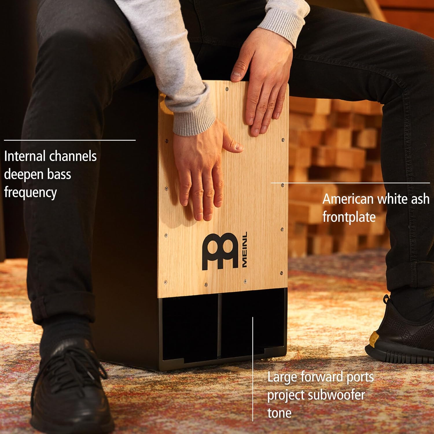 Homem tocando Meinl Subwoofer Cajon com placa frontal branca americana e aberturas para subwoofer na frente.