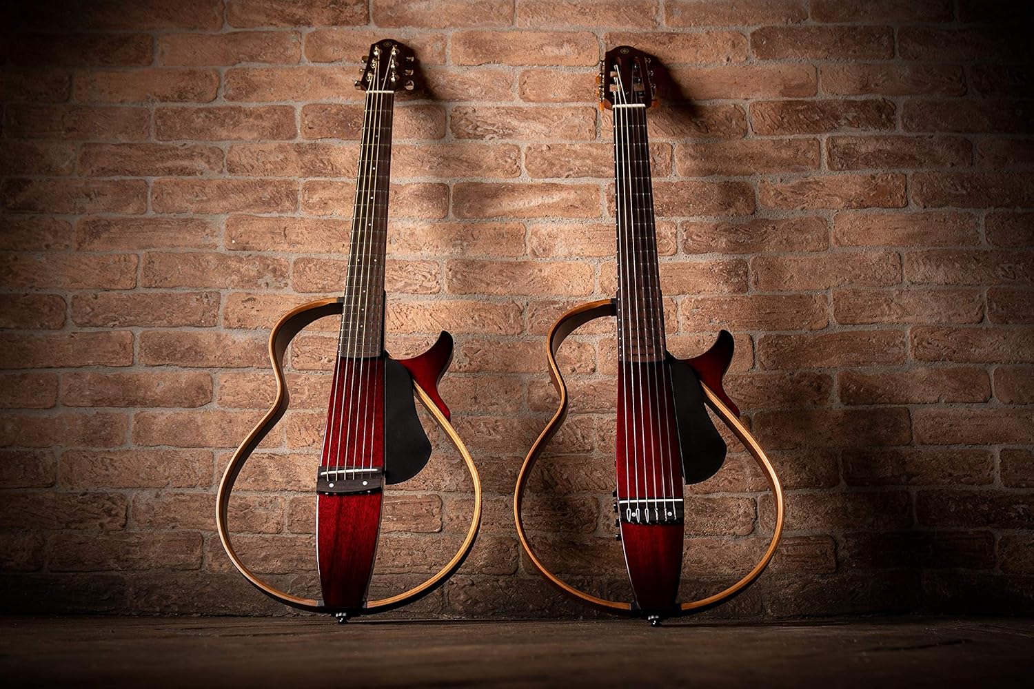 Dois violões Yamaha SLG-200N TBL vermelho translúcido com corpo esqueleto em parede tijolada