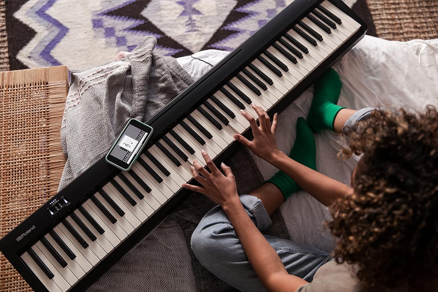 Pessoa tocando piano digital Roland FP-10 BK com smartphone conectado via Bluetooth.
