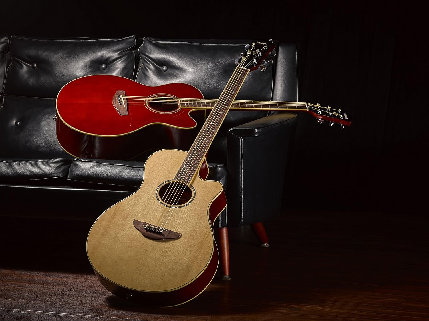 Dois violões Yamaha APX-600 eletroacústicos, um natural com tampo spruce e outro vermelho, apoiados em sofá preto