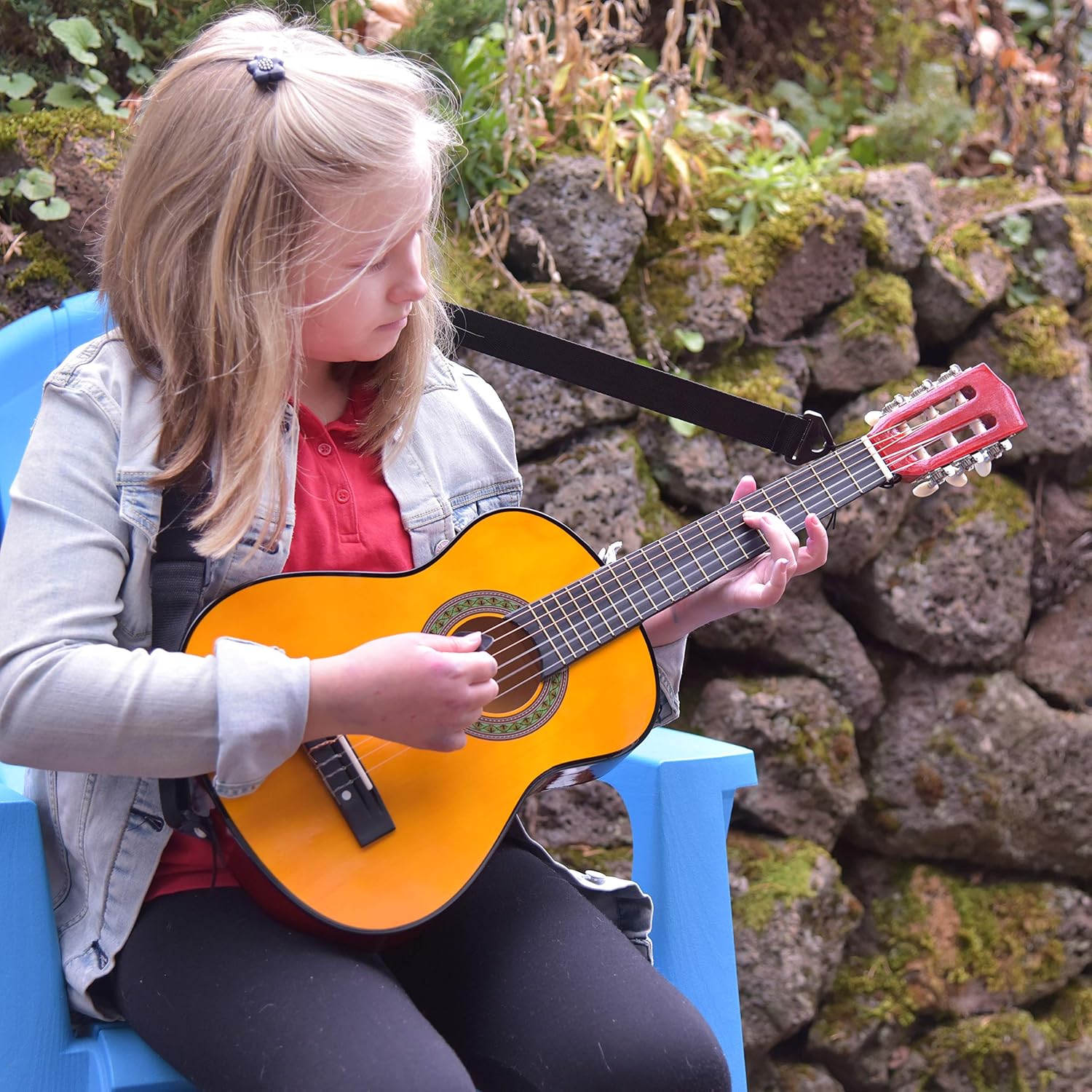 Criança tocando guitarra infantil Master Play sentada em cadeira azul ao ar livre