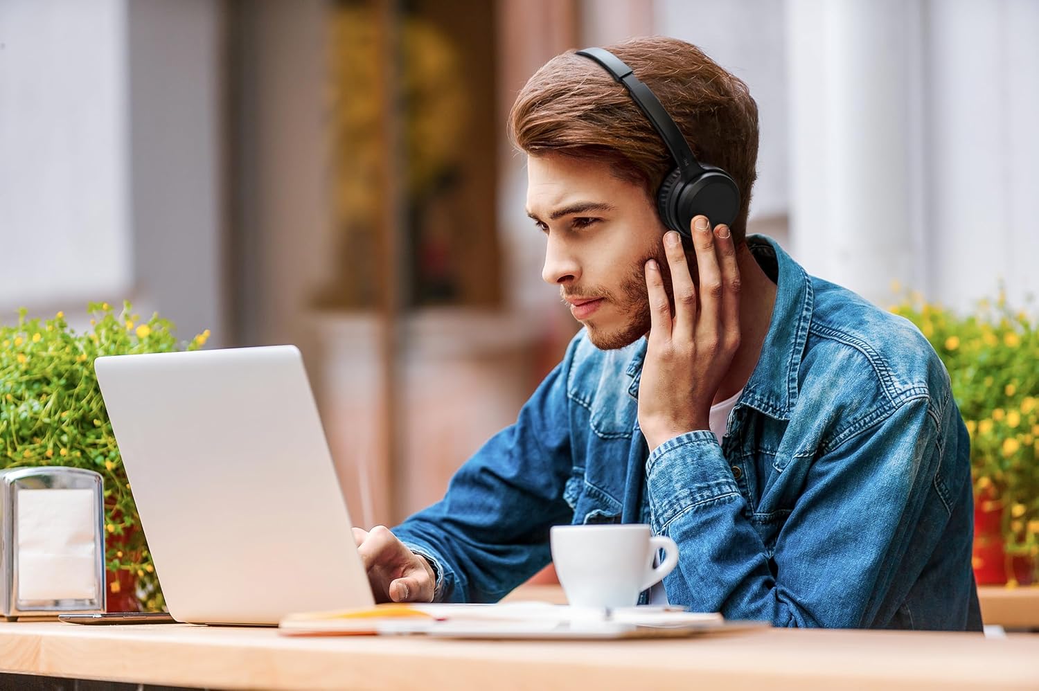 Homem usando headphone Philips TAH1108BK/55 preto on-ear Bluetooth com microfone, trabalhando no laptop