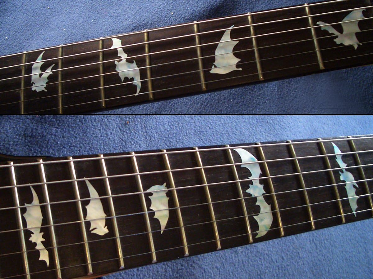 Braço de guitarra com adesivos de morcego em pérola branca aplicados entre os trastes, fundo azul.