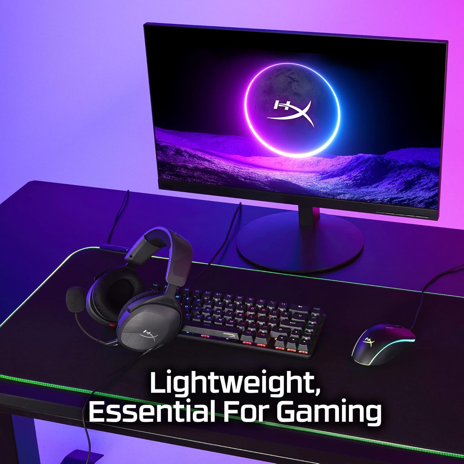HyperX headset displayed on gaming desk setup with illuminated monitor and RGB keyboard.